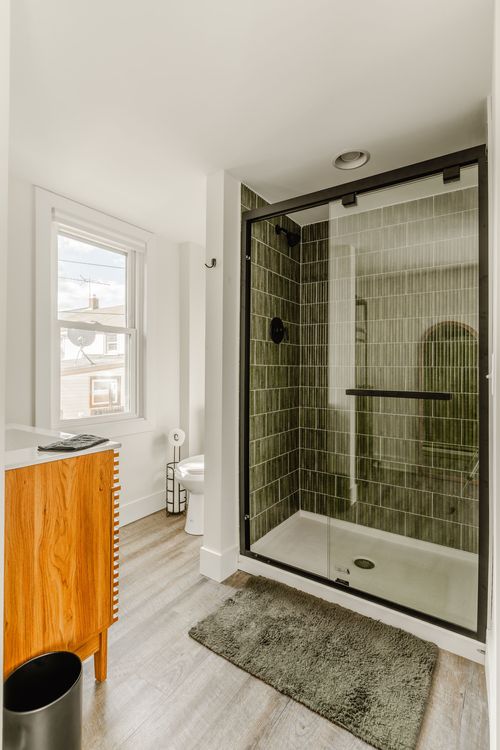 Bathroom with a black-framed glass shower, green tile and wood dresser