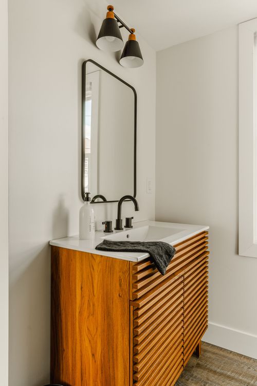 Fluted wood vanity with a black-framed mirror and two-light black sconce