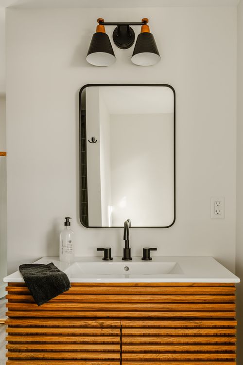 Close view of a fluted wood vanity with black faucet and framed mirror