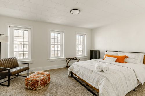 Bedroom with three windows, a leather chair, orange pouf and striped bedding