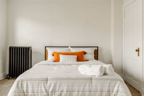 Bed with white linens, orange pillows and rolled towels beside a paneled white door