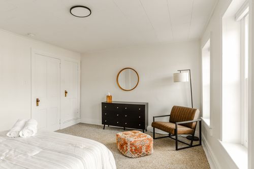 Bedroom corner with black dresser, round mirror, leather armchair and orange patterned pouf