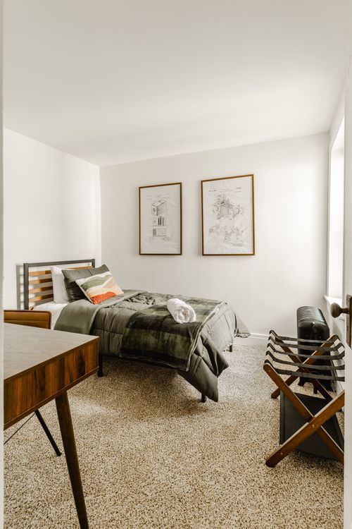 Narrow bedroom with a slatted headboard twin bed, framed patent prints and a wood desk