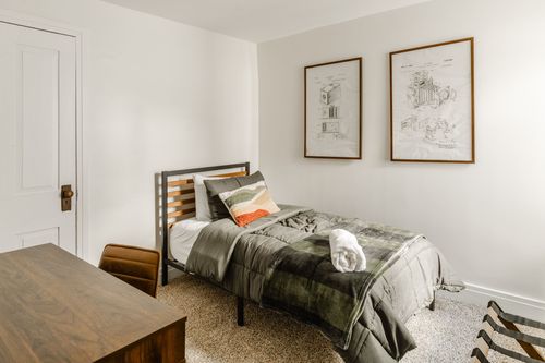 Twin bed with framed patent prints above and a leather desk chair nearby