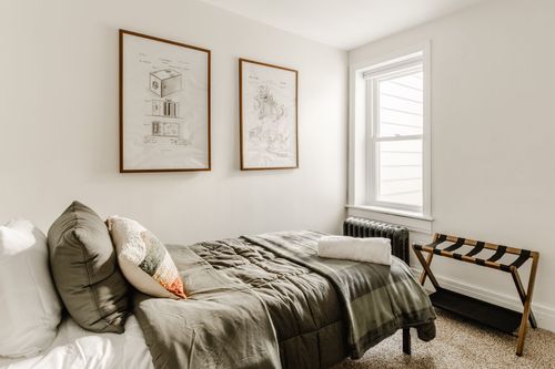 Twin bed with olive bedding, framed prints, a window and a folding luggage rack