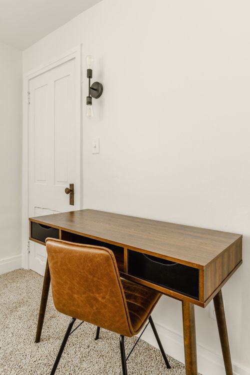 Wood desk with drawers, a leather chair and a wall sconce beside a white door