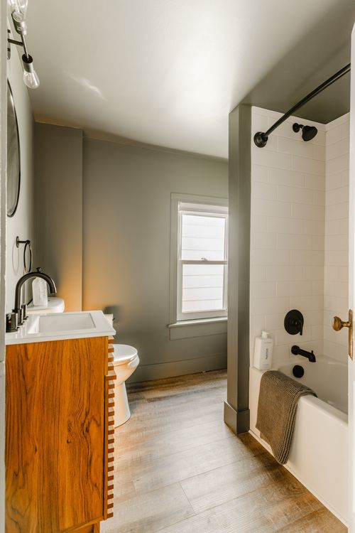 Bathroom with a wood-slat vanity, oval mirror and a tiled tub-shower combo