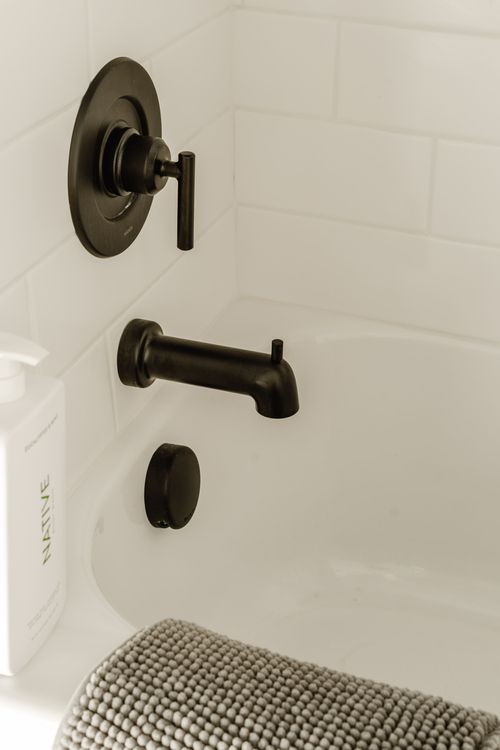 Close-up of matte black tub fixtures against white subway tile