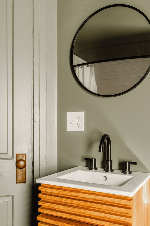 Bathroom vanity with round black-framed mirror, wood slats and sage green walls