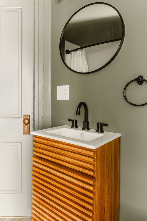 Bathroom sink with round mirror, black towel ring and slatted wood vanity
