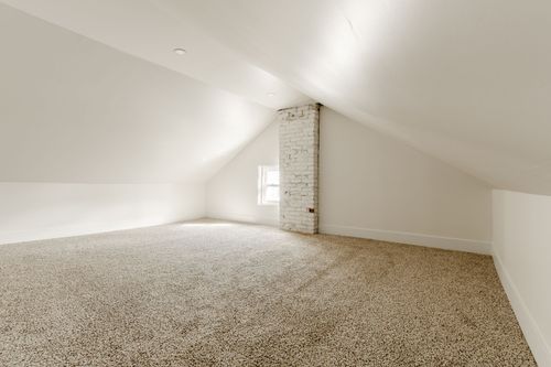 Empty attic loft room with sloped ceilings, carpet and an exposed brick chimney