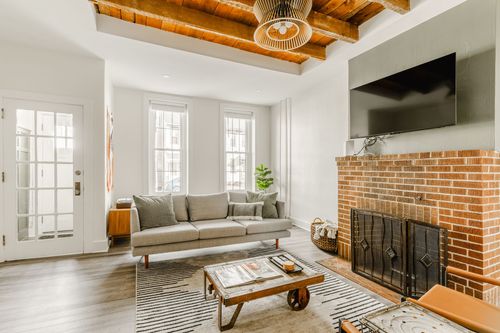 Living room with a wood beam ceiling, woven pendant light, linen sofa and brick fireplace