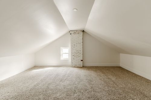 Vaulted attic loft with carpet flooring, a small window and brick chimney stack