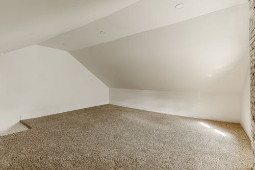 Empty sloped-ceiling attic room with wall-to-wall carpet