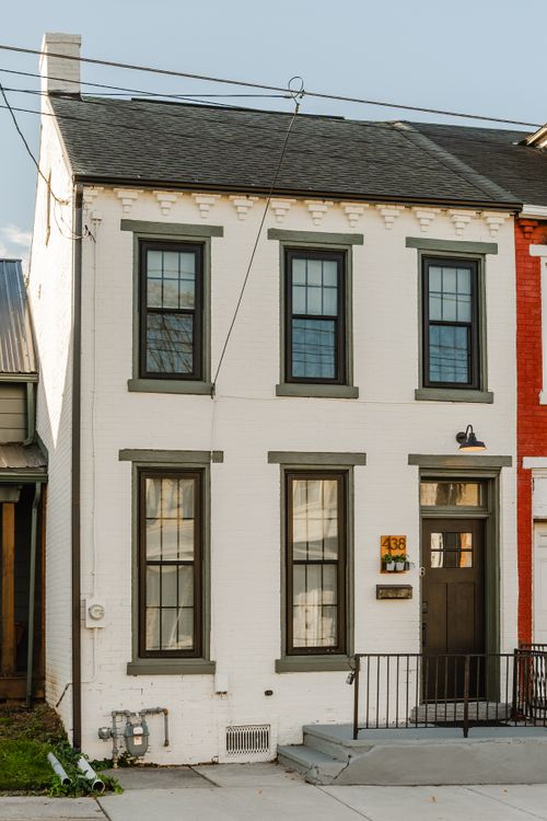 White brick rowhome facade with sage green window trim and a dark wood front door