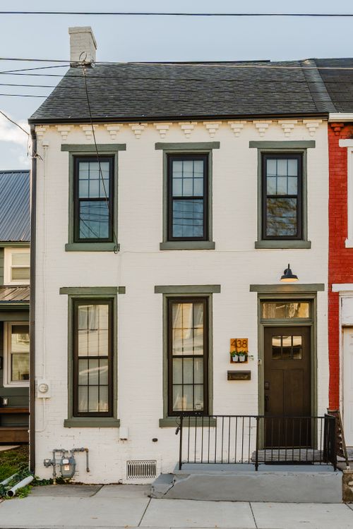 Two-story white brick rowhome with green-trimmed windows and an iron porch rail