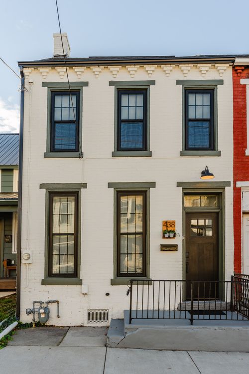 Rowhome facade in warm evening light with white brick, green trim and a house number by the door
