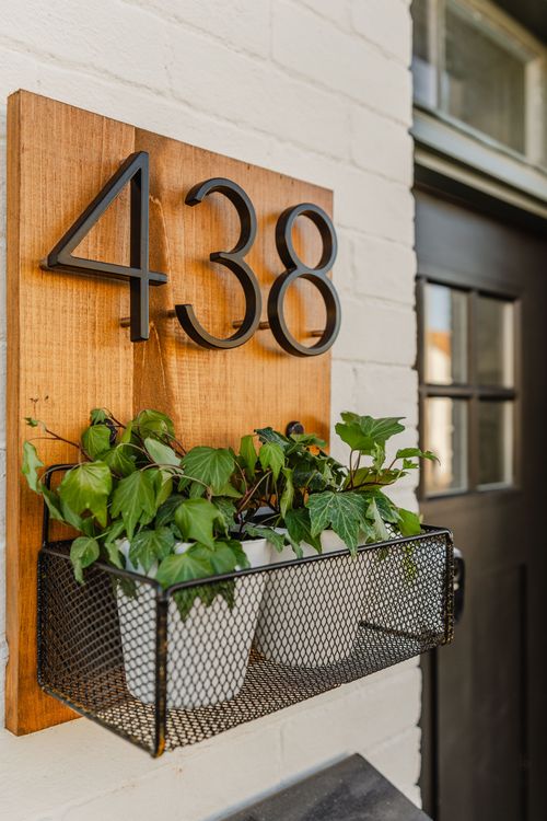 House number sign mounted on wood with a hanging planter of trailing ivy by a black door