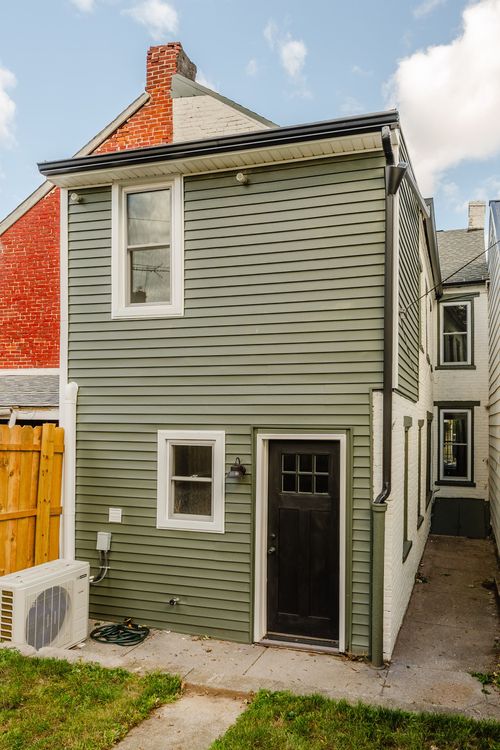 Rear exterior of a house with sage green siding, a black door and white trim