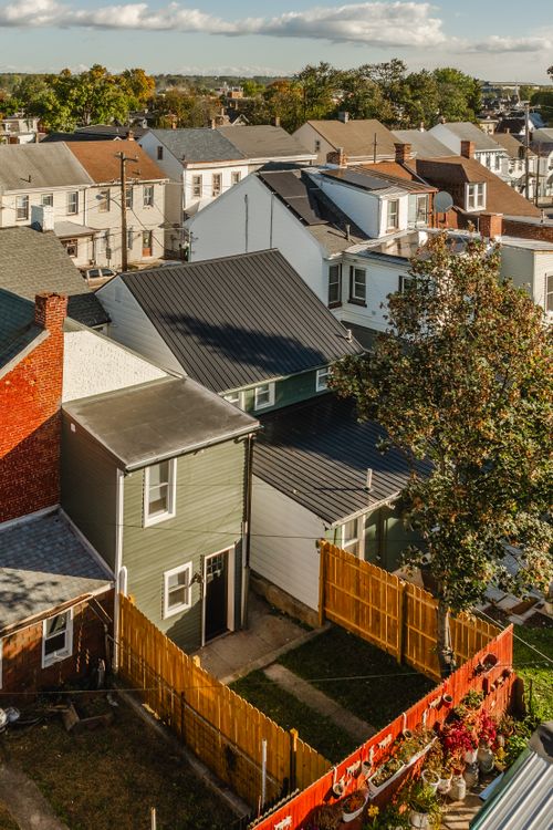 Aerial view of a green house with a black metal roof and a wood-fenced backyard