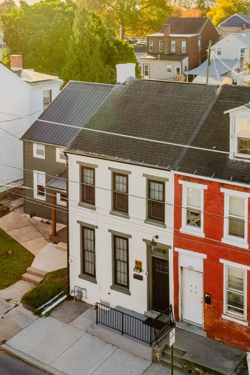 Aerial view of a green house roofline with metal roofing and a fenced yard below