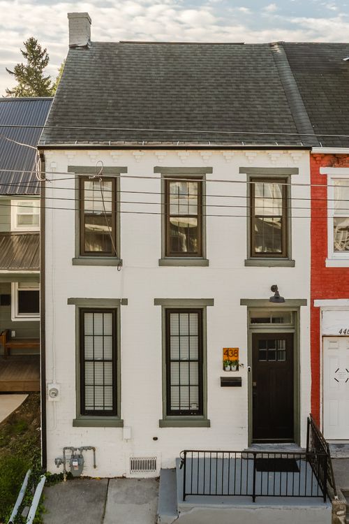 Aerial view of a white house with a dark roof beside a red brick rowhome