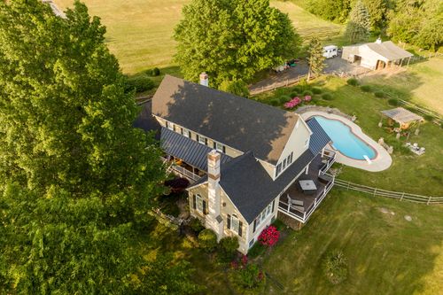 Aerial view of a stone-and-shingle farmhouse with a pool and manicured lawn