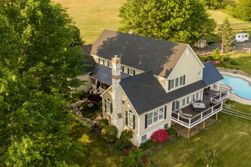 Aerial view of a farmhouse with metal roof, pool and horse pasture beyond