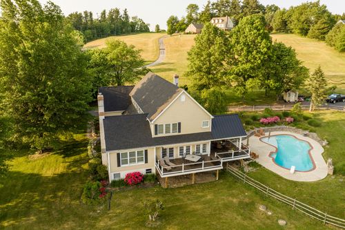 Aerial view of a farmhouse with covered deck, pool and rolling countryside