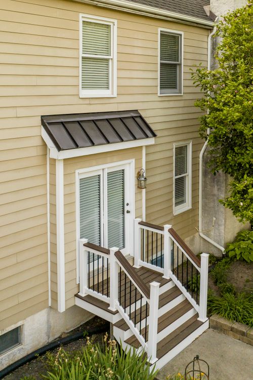 Rear exterior of a house with a metal-roofed door awning and a wood deck staircase