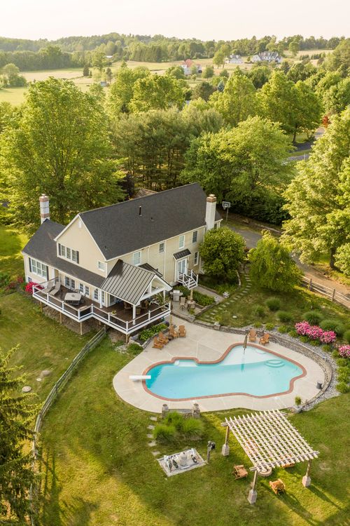 Aerial view of a farmhouse with pool, stone patio and a pergola surrounded by countryside