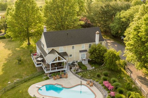 Aerial view of a farmhouse with a kidney-shaped pool, deck and long gravel driveway