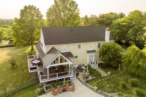 Aerial view of a farmhouse with covered porch, patio and free-form pool