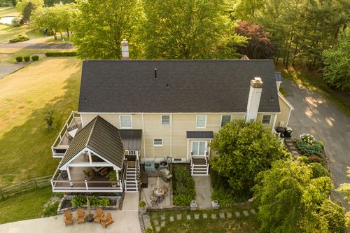 Aerial view of a farmhouse with covered porch, pool and curved driveway