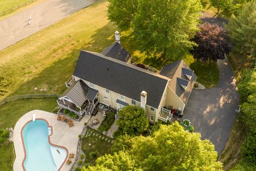 Aerial view of a farmhouse with a free-form pool, mature trees and gravel driveway