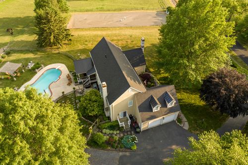Aerial view of a farmhouse with a two-car garage, dormer windows and distant riding arena
