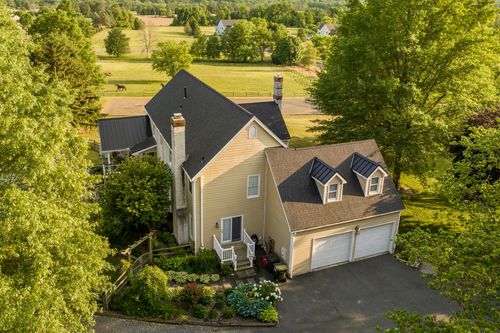 Aerial view of a farmhouse beside a horse pasture with dormer windows and attached garage