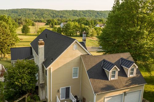 Aerial view of a farmhouse with stone chimney, dormer windows and two-car garage