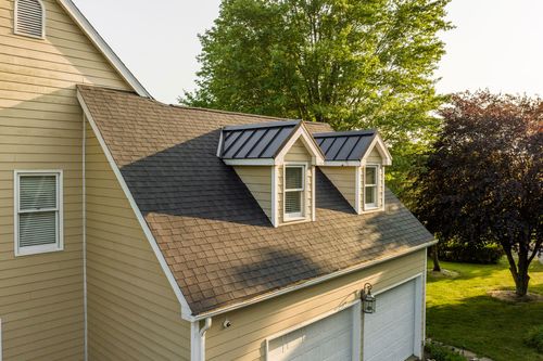 Close-up of a shingled roofline with two shed dormers above a two-car garage