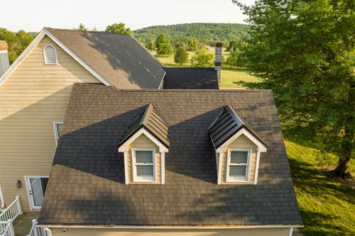 Aerial close-up of matching gable dormers on a shingle roof with hills in the distance