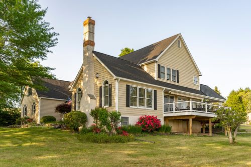 Farmhouse exterior with a tall stone chimney, American flag and red flowering shrubs