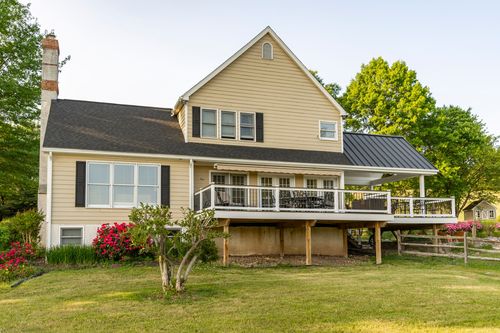 Rear exterior of a farmhouse with a covered deck and blooming azaleas