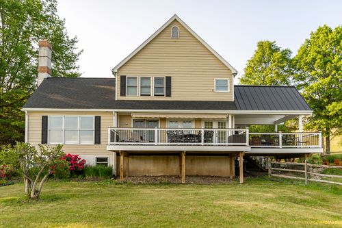 Rear exterior of a farmhouse with a wraparound deck and standing-seam porch roof