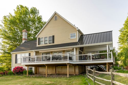 Rear exterior of a farmhouse with a wraparound porch, standing-seam roof and stone chimney