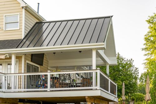 Covered porch with a standing-seam metal roof and wicker seating overlooking a deck