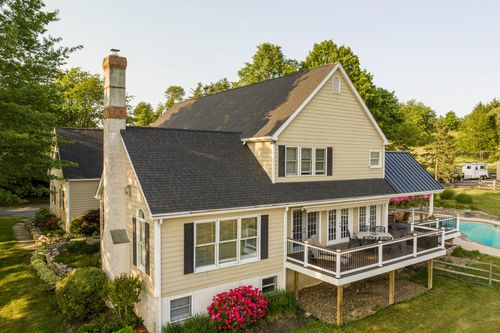 Farmhouse exterior at dusk with an American flag, wraparound porch and standing-seam roof