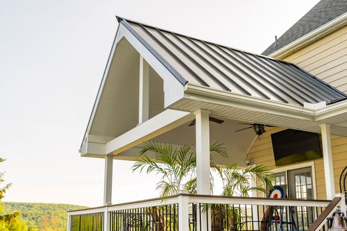 Vaulted porch ceiling with a ceiling fan, potted palms and a standing-seam metal roof