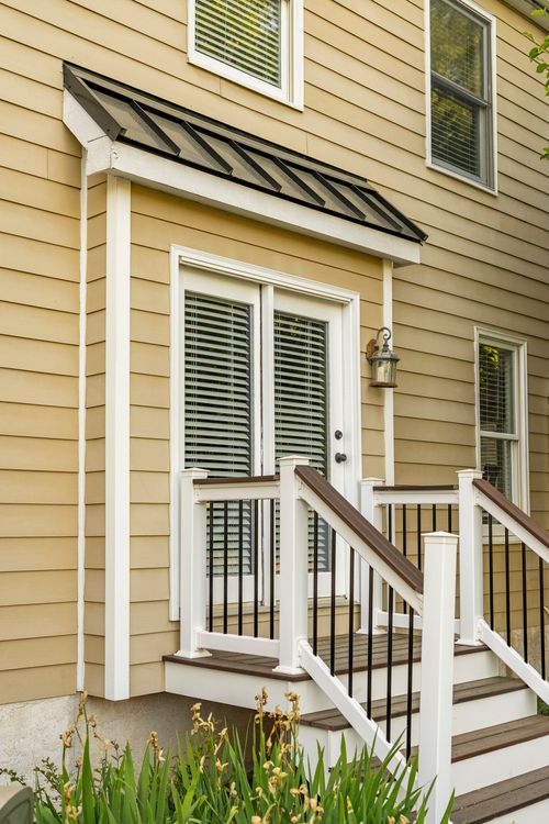 Close-up of a rear French door with a black standing-seam awning and deck railing