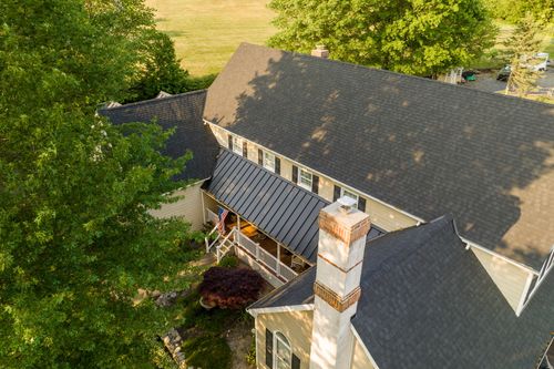Aerial view of a farmhouse chimney and covered porch with a standing-seam metal roof